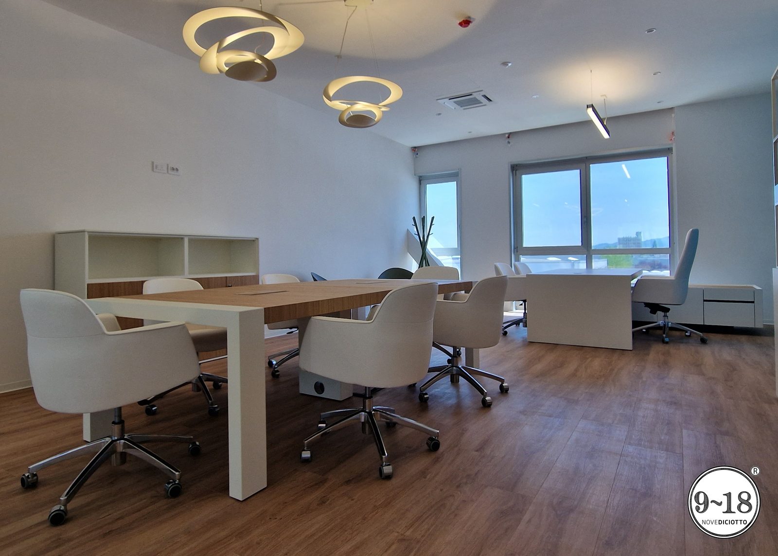 Sala riunioni con tavolo in legno, sedute avvolgenti e illuminazione di design.
